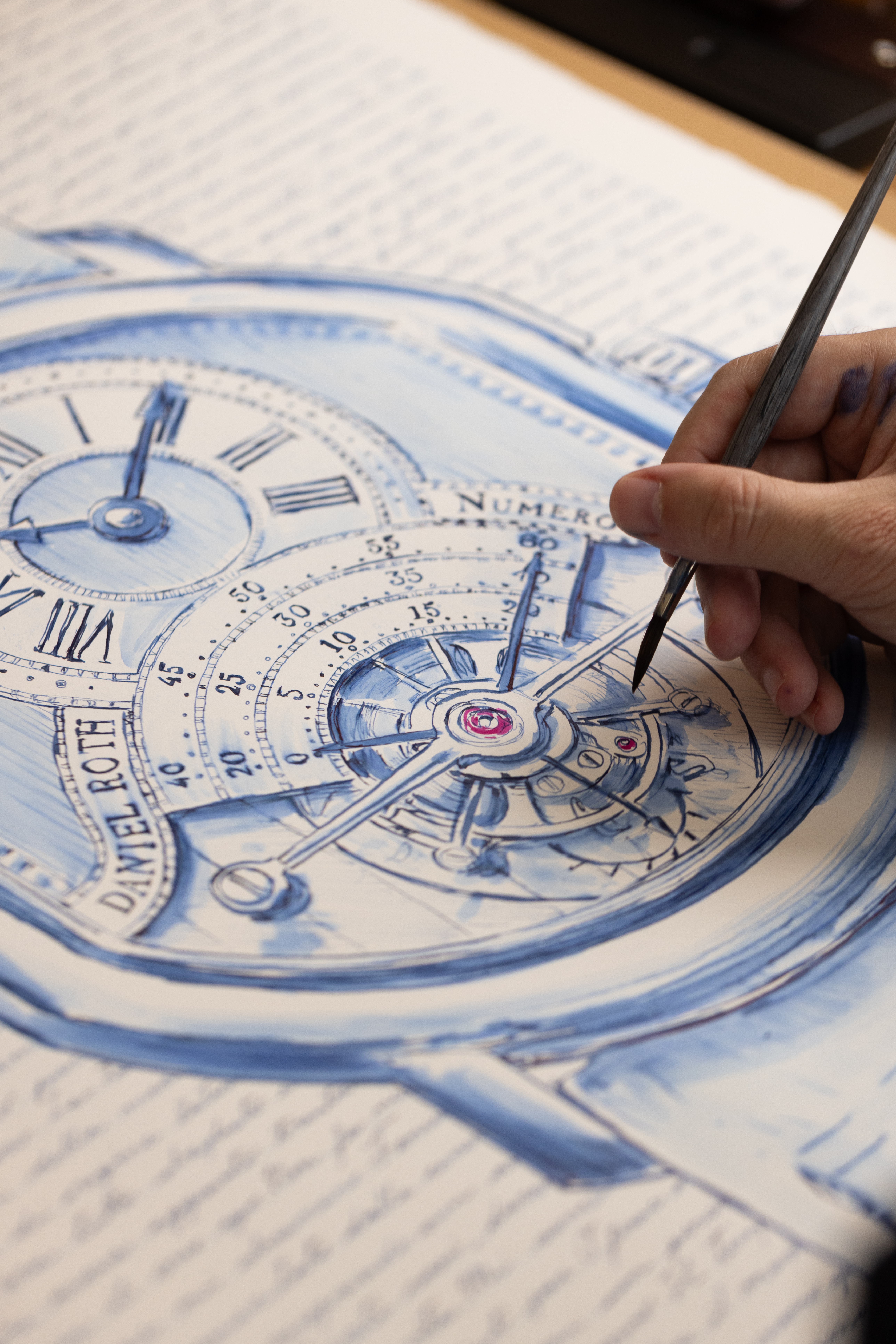 Close view of a brush drawing the tourbillon mechanism in blue ink.