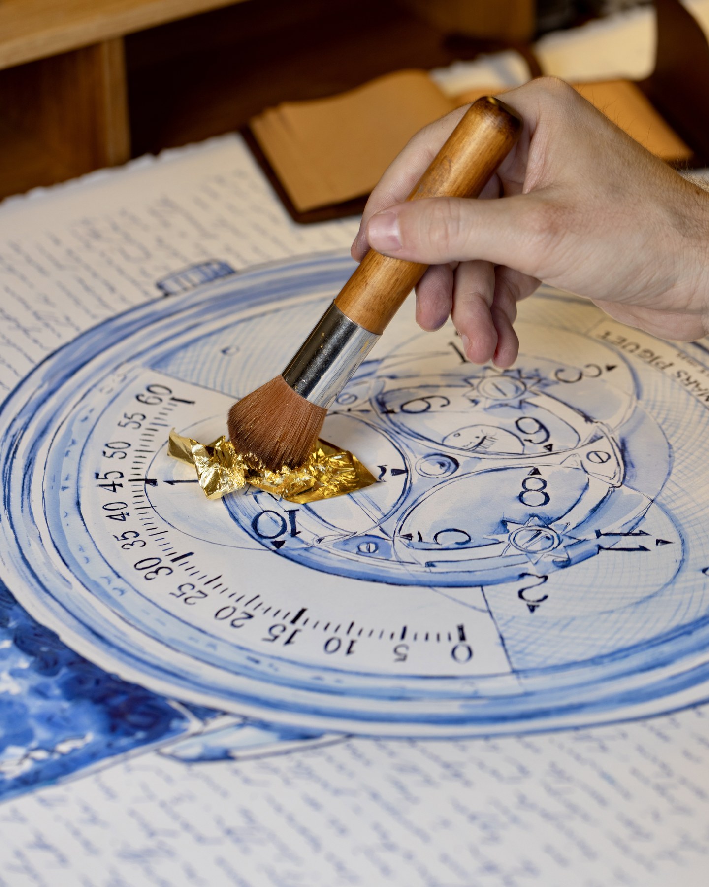 A broad brush pressing gold leaf onto the Star Wheel dial drawing.