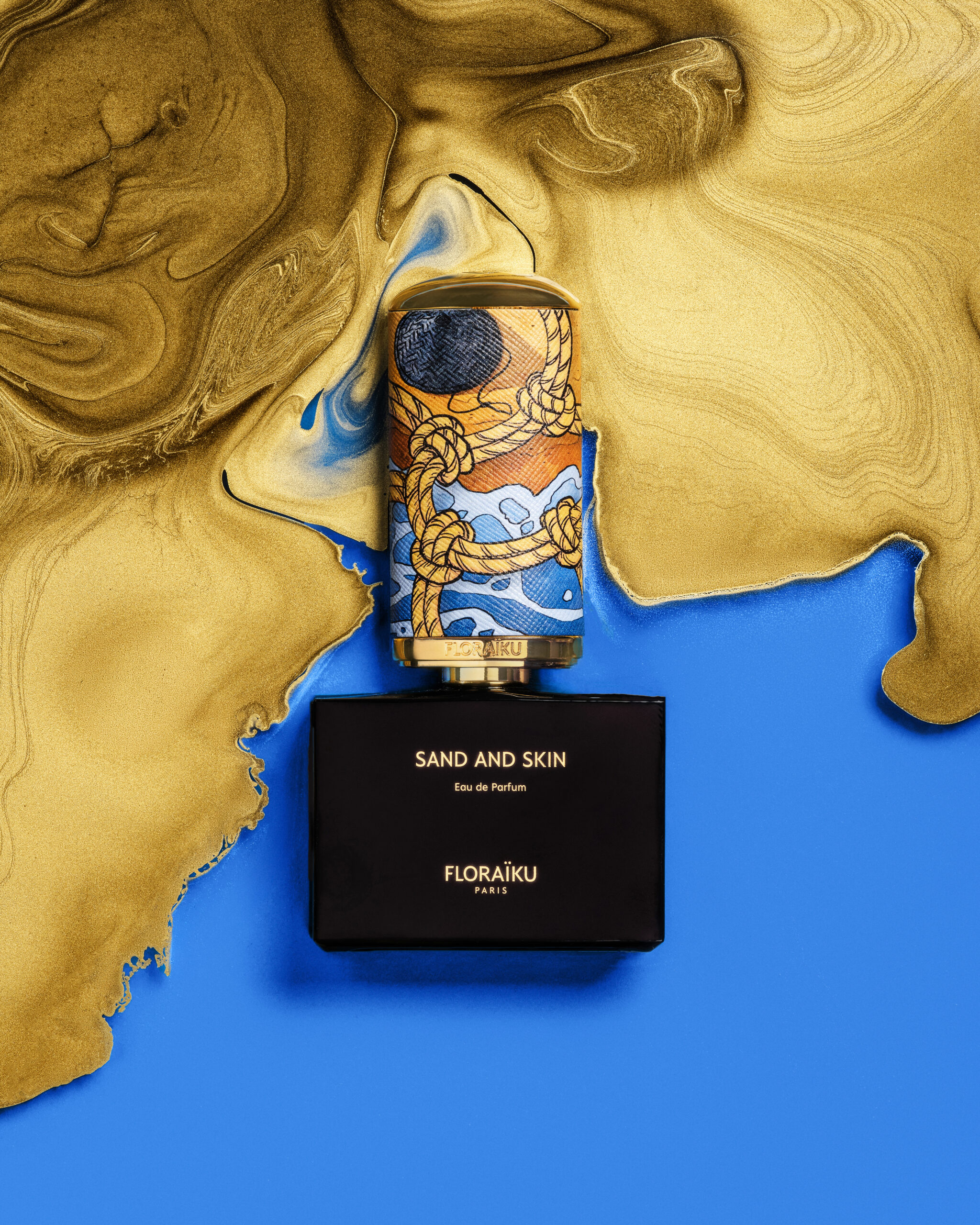 Floraïku Sand and Skin bottle and case with Mauro Carraro's cap illustration, set in blue and liquid gold.