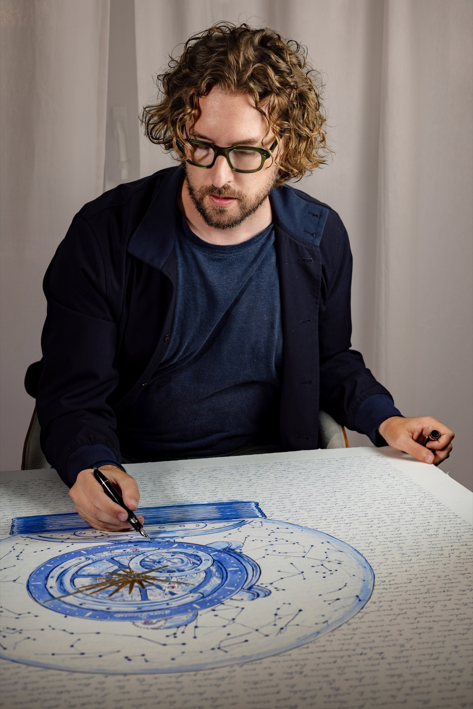 Mauro Carraro drawing Atmos at his atelier desk, with the handwritten letter surrounding the celestial composition.