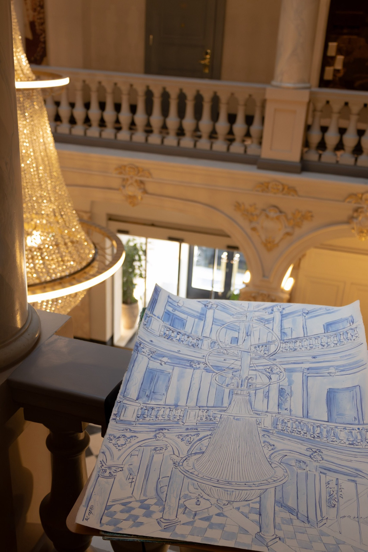 Blue-ink drawing of the Ritz-Carlton Geneva chandelier, held beside the chandelier it depicts.